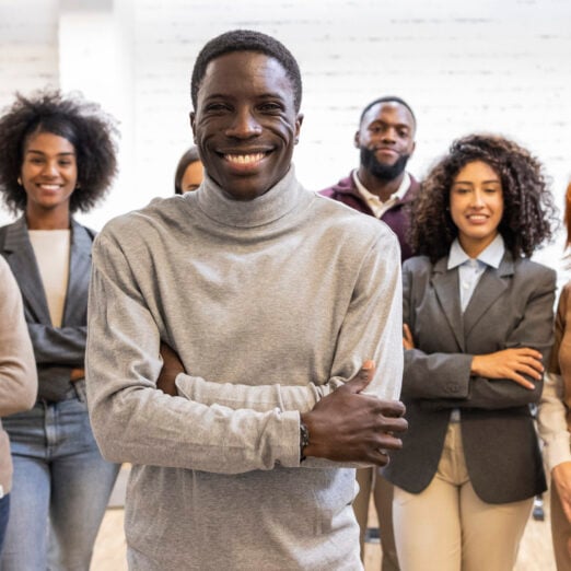 Happy multi ethnic businesspeople standing together in modern coworking office with arms crossed, smiling, looking at camera, showing teamwork, unity, diversity and cooperation