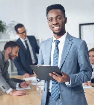 african american businessman with clipboard in conference hall with blurred colleagues on background